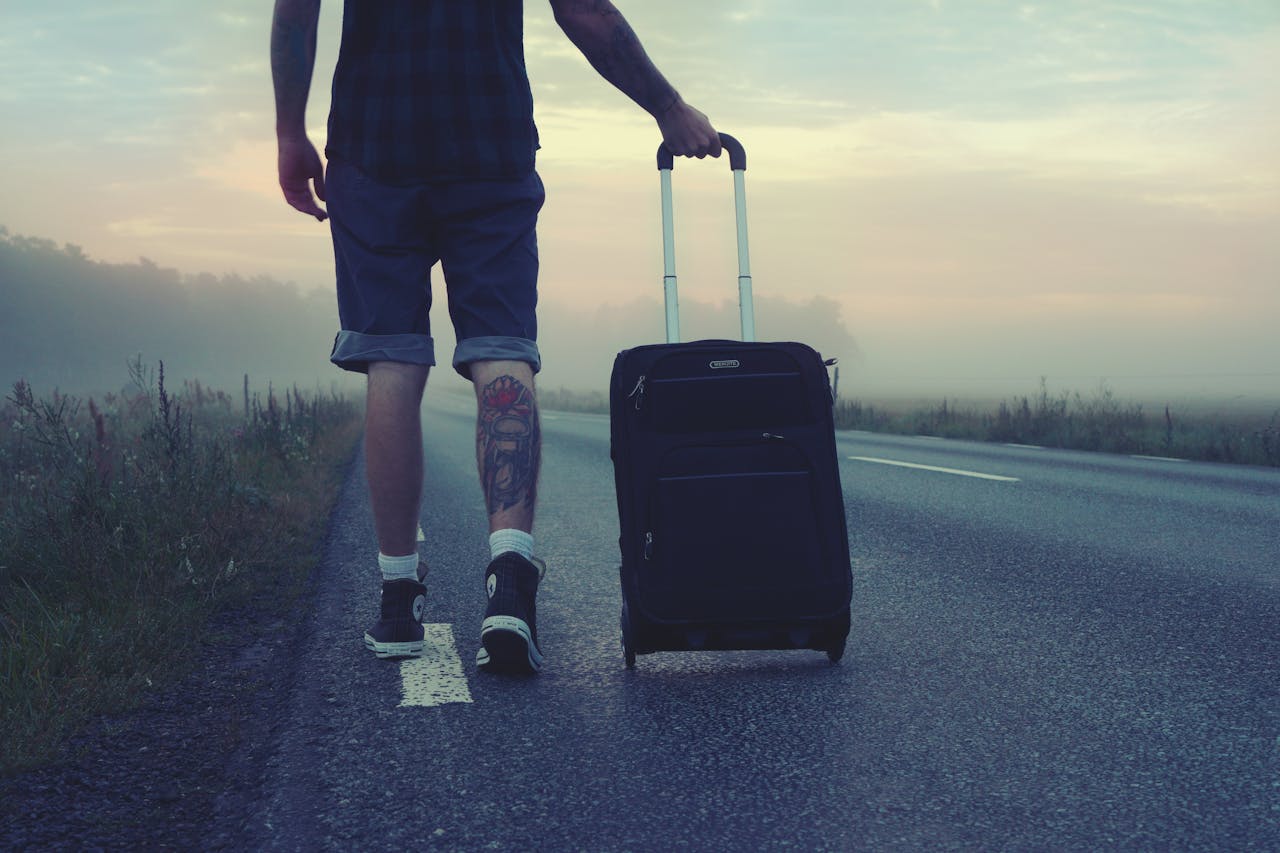 Man walking with a suitcase along a foggy road at sunrise, symbolizing adventure and travel.